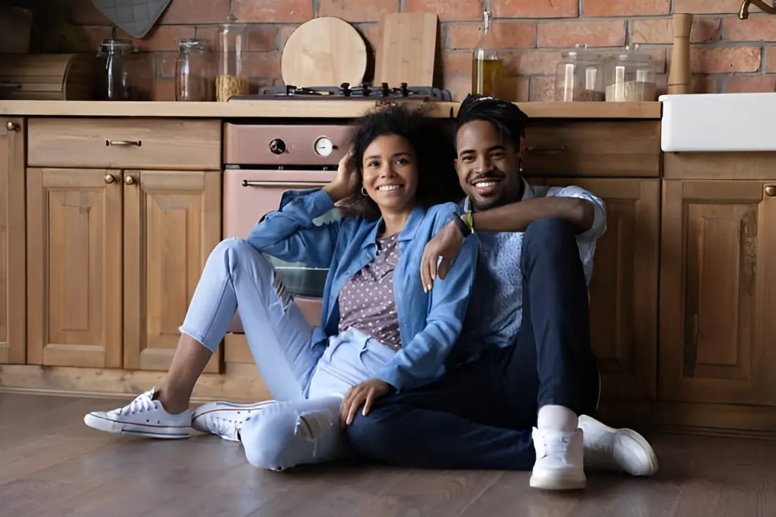 A man and woman sitting on the floor in front of a stove.